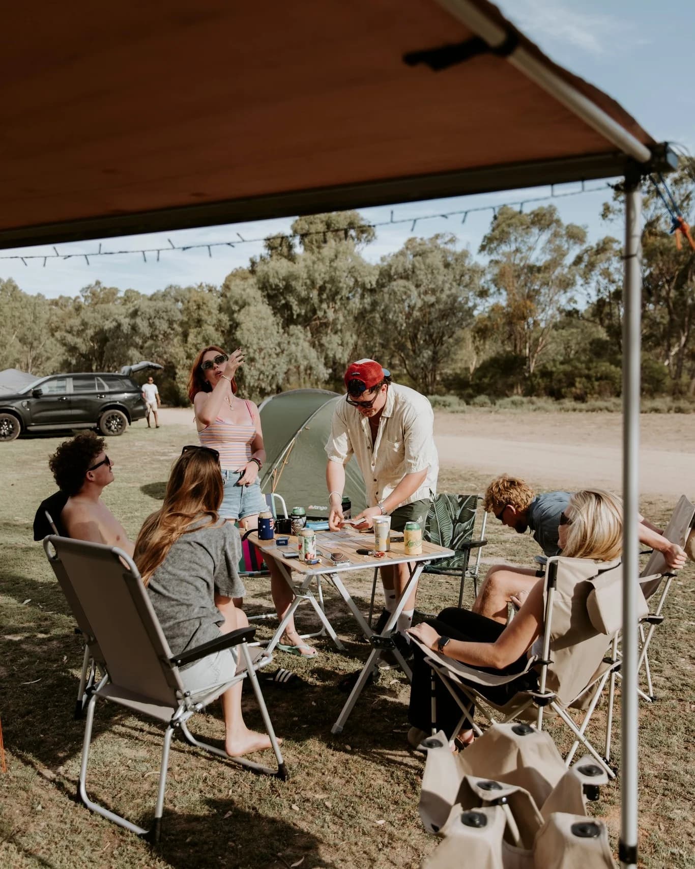 Friends gathered around a table at their campsite, with a tent behind them