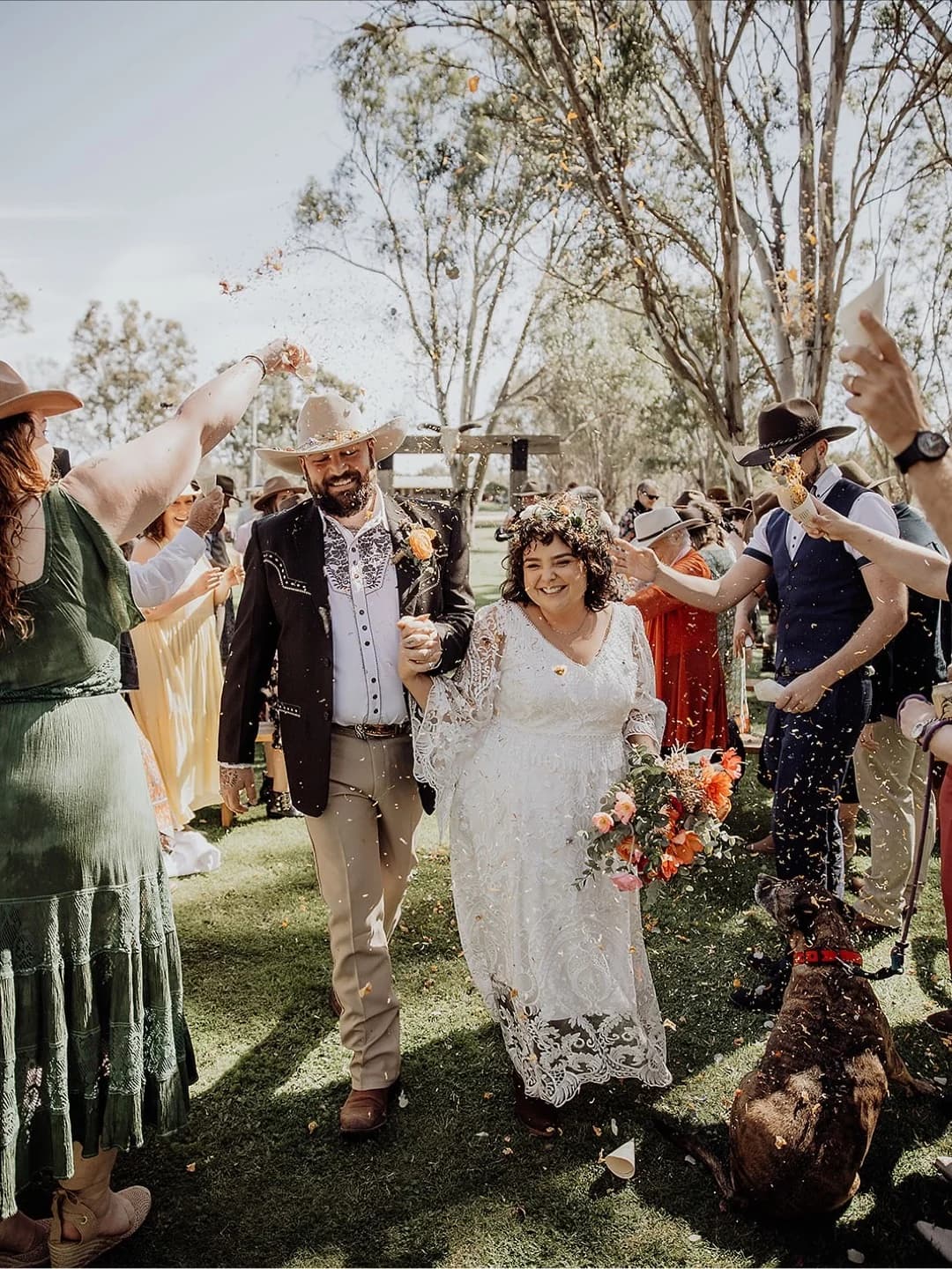 Wedding guests throwing confetti around the couple, with their dog beside them